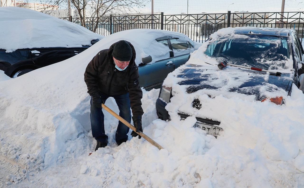 человек откапывает машину от снега